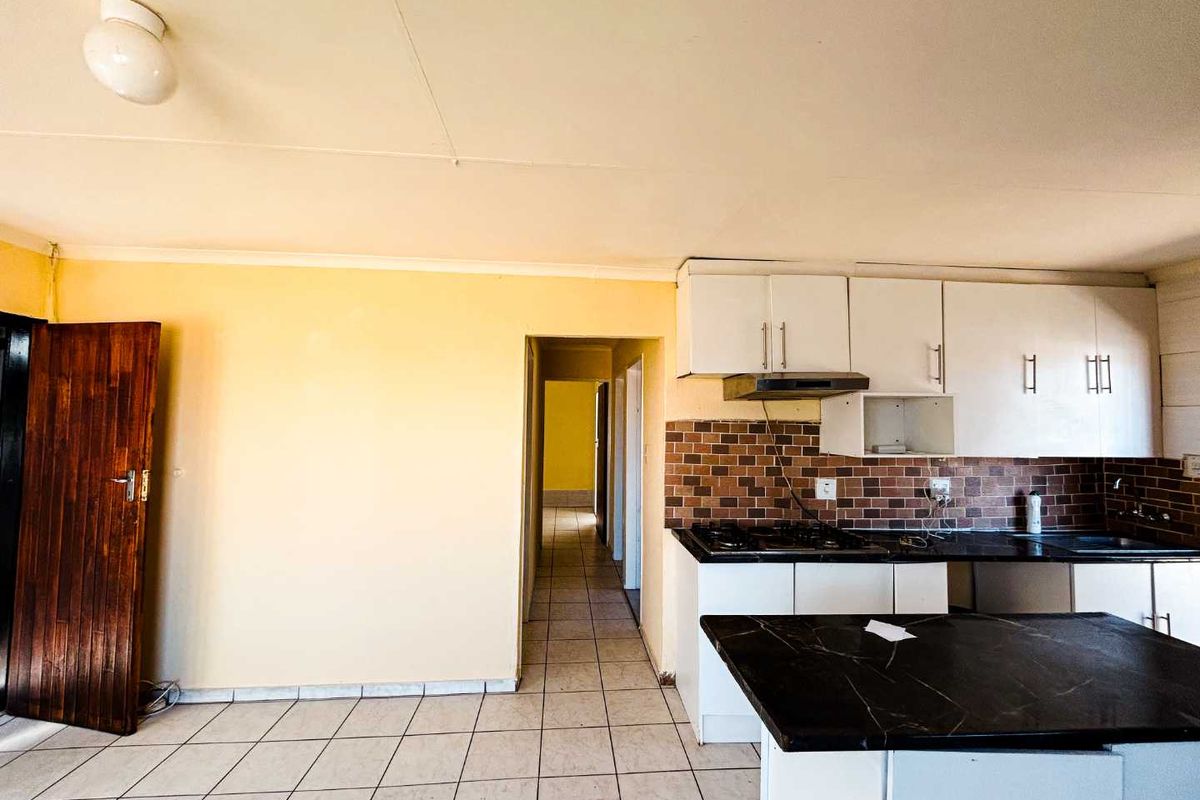 A functional kitchen featuring built-in cabinetry, a gas hob with extractor fan, tiled backsplash, and dark countertops, leading into a hallway.