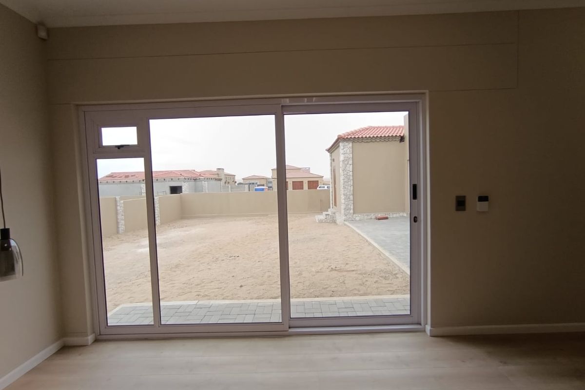 Interior view looking out through large sliding glass doors to a spacious, undeveloped backyard area with paved patio section.
