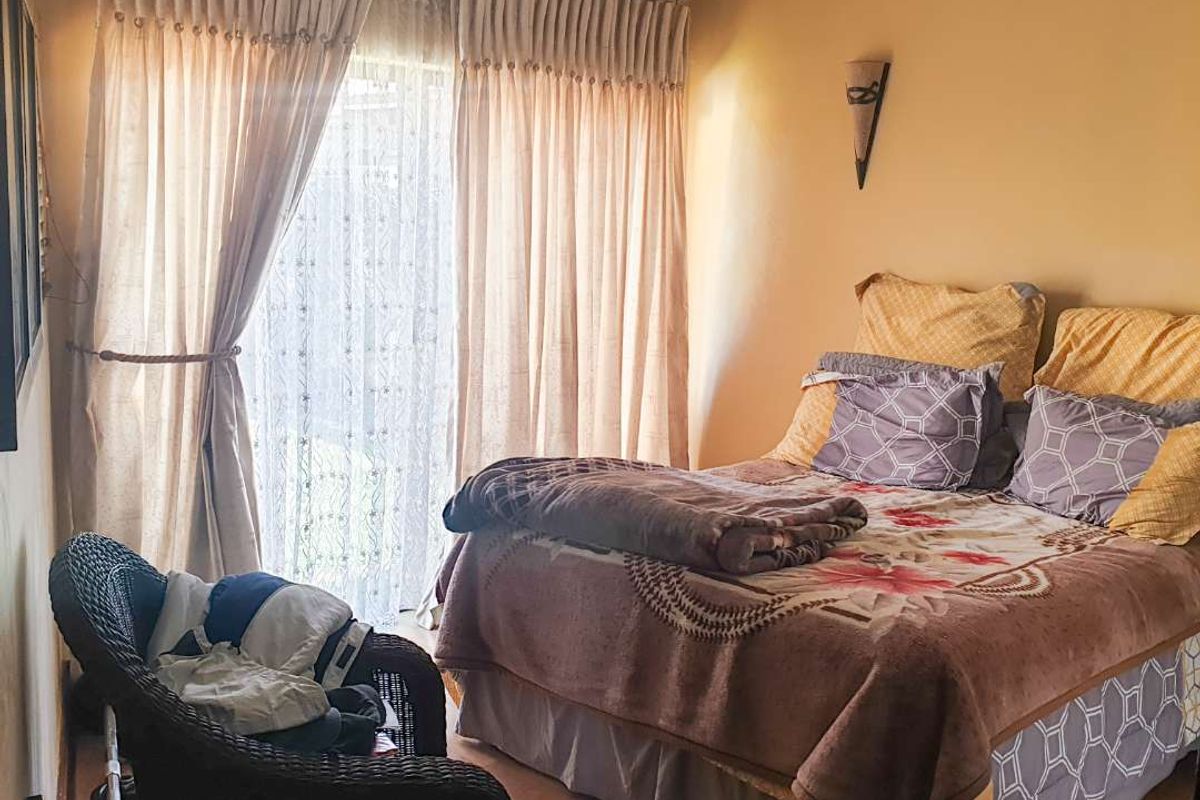 A cozy bedroom featuring laminate flooring, a wall sconce, and a sliding glass door with floor-to-ceiling curtains providing natural light.