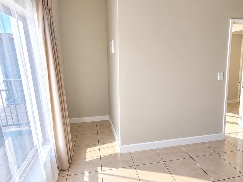 A bright, empty living area featuring neutral wall tones, tiled flooring, and a large sliding glass door providing access to the balcony.