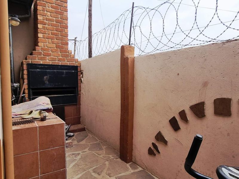 Outdoor patio area featuring a built-in brick braai, stone paving, and high perimeter walls secured with razor wire.