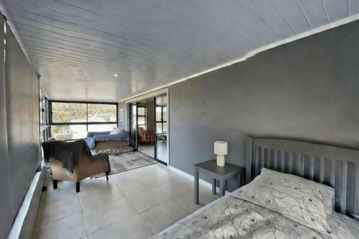 Spacious bedroom featuring tiled flooring, a painted timber ceiling, and large windows with sliding door access to an adjoining sunroom area.
