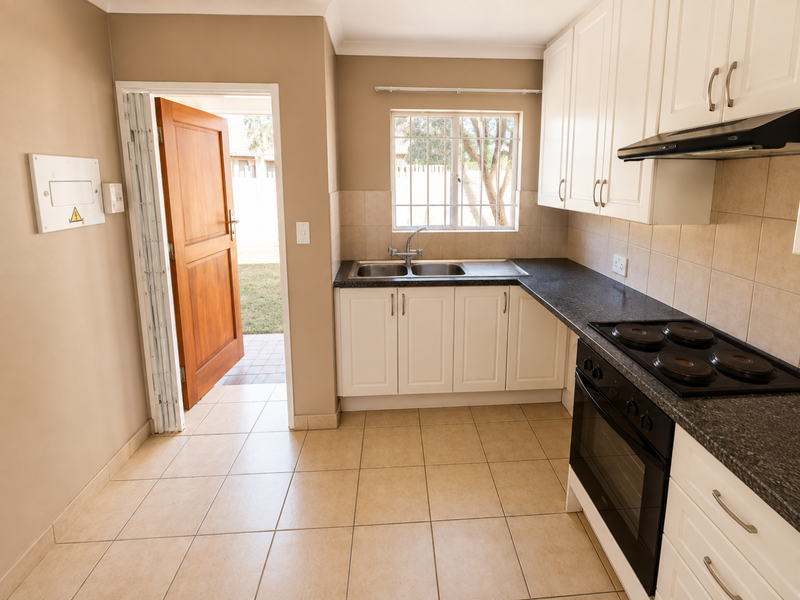 A clean, functional kitchen featuring white cabinetry, dark countertops, built-in oven and hob, tiled flooring, and direct access to the rear exterior.