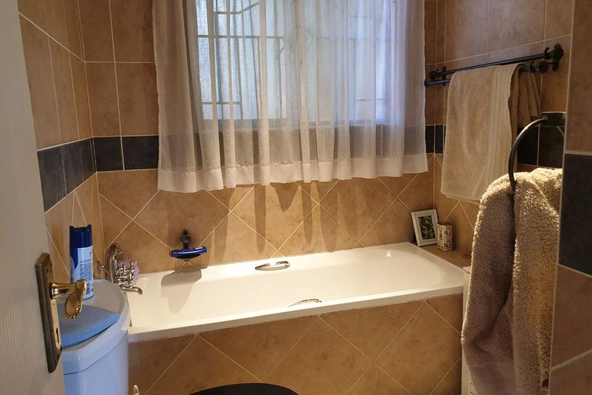 A functional bathroom featuring a built-in bathtub with tiled surround, wall-mounted fixtures, and a window with security bars.