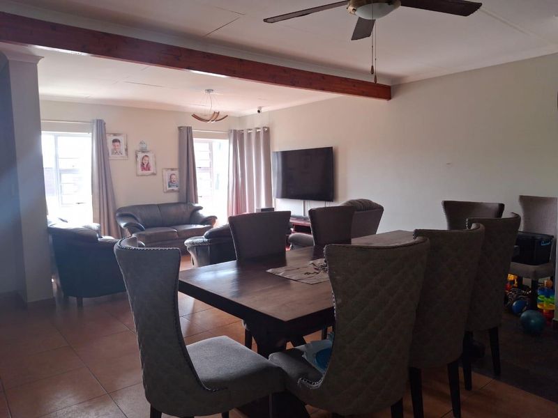 Spacious open-plan living and dining area featuring tiled flooring, a ceiling fan, and an exposed timber beam detail.
