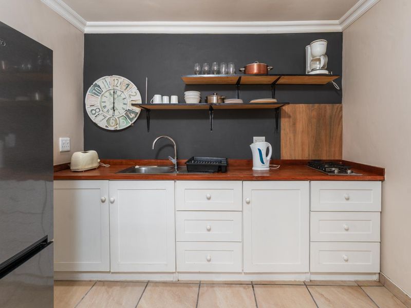 A compact kitchen featuring white cabinetry, a wooden countertop, a gas hob, and open shelving against a dark accent wall.