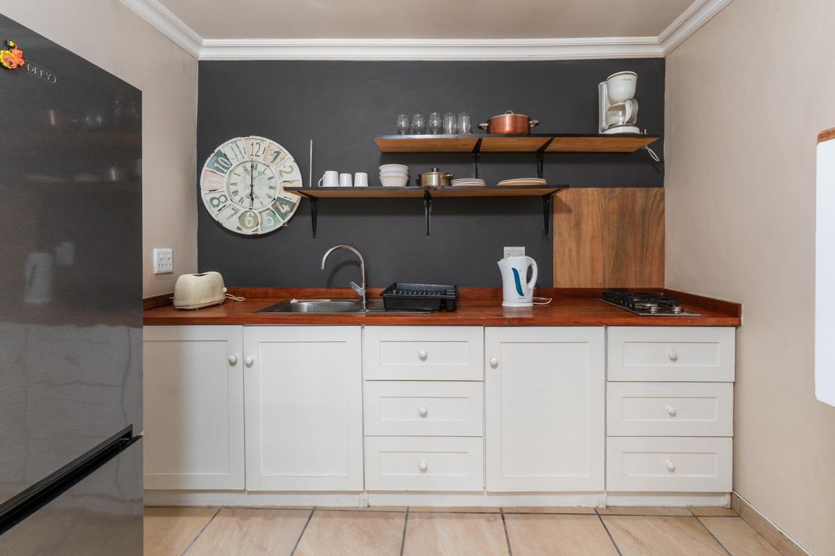 A compact kitchen featuring white cabinetry, a wooden countertop, a gas hob, and open shelving against a dark accent wall.