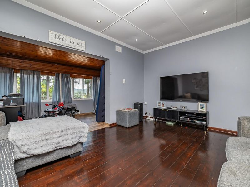 Spacious living room featuring dark timber flooring, recessed downlighting, and a distinct timber-paneled ceiling section, offering a versatile layout for family relaxation.