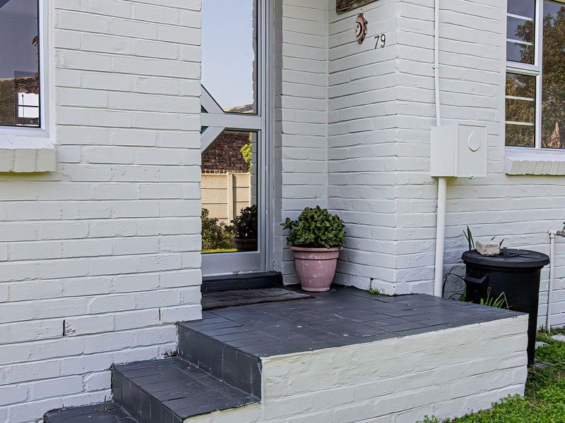 Front entrance of a house featuring a painted brick facade, tiled steps, and aluminium framed windows.