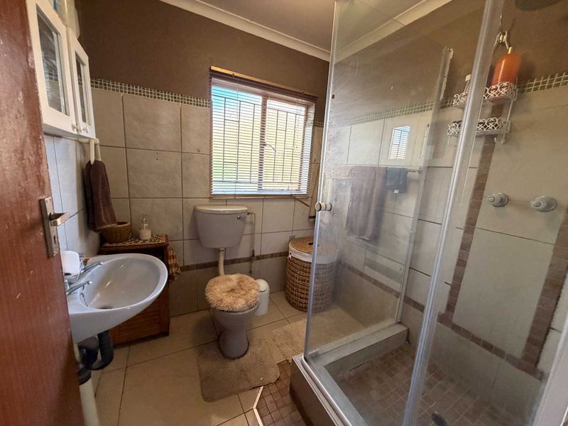 A functional bathroom featuring a shower enclosure, pedestal washbasin, and toilet with tiled finishes throughout.