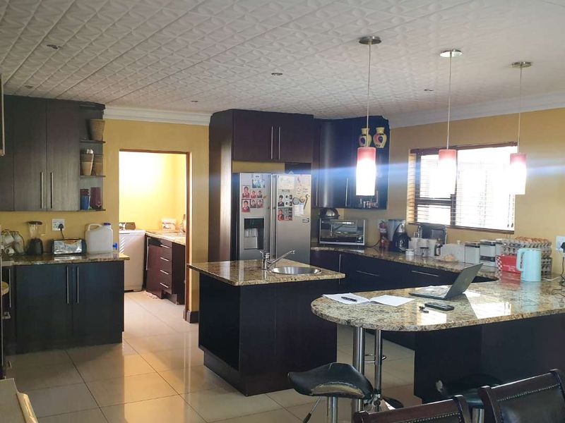 Spacious kitchen featuring dark wood cabinetry, granite countertops, a central island with breakfast bar, and tiled flooring, with an adjacent scullery area.