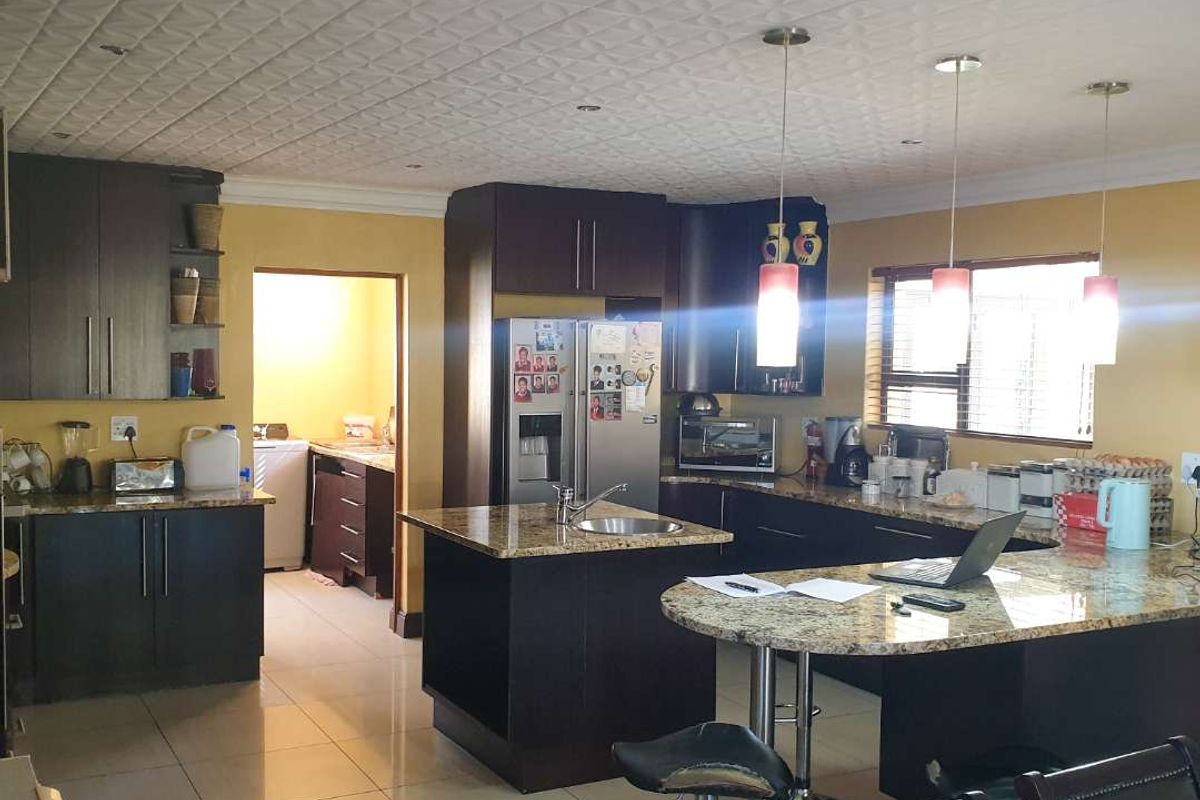 Spacious kitchen featuring dark wood cabinetry, granite countertops, a central island with breakfast bar, and tiled flooring, with an adjacent scullery area.