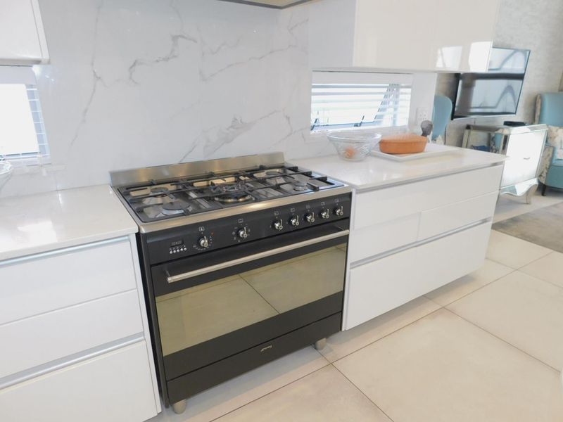 Modern kitchen featuring a high-end gas stove, sleek handleless cabinetry, quartz countertops, and a stylish marble-look splashback.