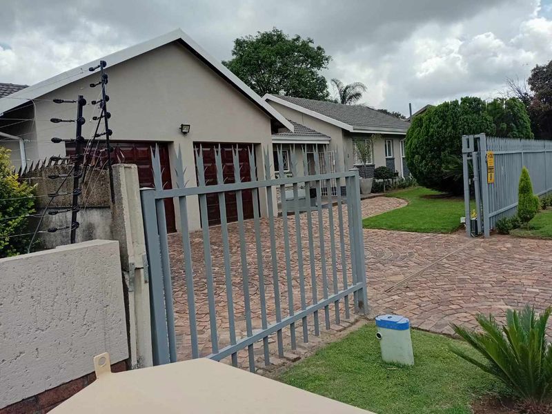 Front view of a residential property featuring a double garage, paved driveway, and secure gated entrance with established garden and electric fencing.