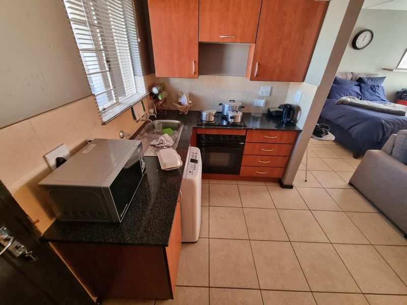 Compact kitchen featuring laminate cabinetry, granite countertops, built-in oven, electric hob, and tiled backsplash, adjacent to an open-plan living and bedroom area.