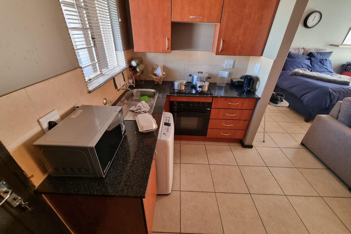 Compact kitchen featuring laminate cabinetry, granite countertops, built-in oven, electric hob, and tiled backsplash, adjacent to an open-plan living and bedroom area.