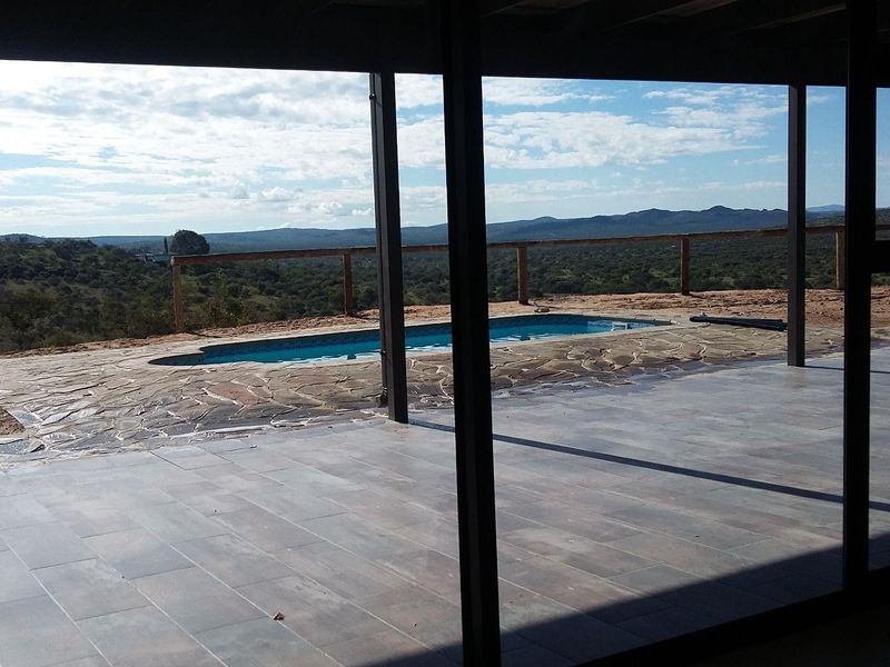 Covered patio area overlooking a swimming pool with stone paving and expansive rural views.