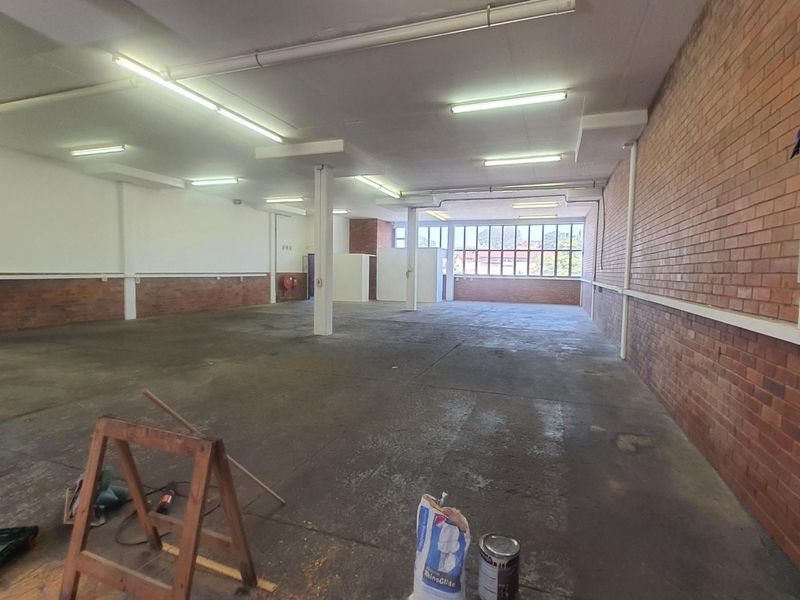 A spacious, open-plan industrial utility area featuring exposed brick walls, concrete flooring, and functional overhead fluorescent lighting, suitable for various commercial or storage uses.