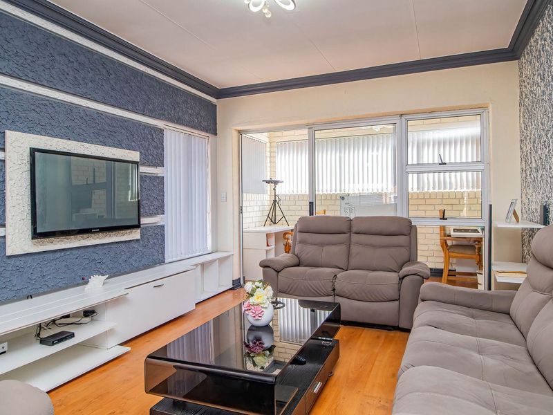 A comfortable living room featuring laminate flooring, a textured accent wall with a built-in media console, and sliding glass doors leading to an enclosed patio.