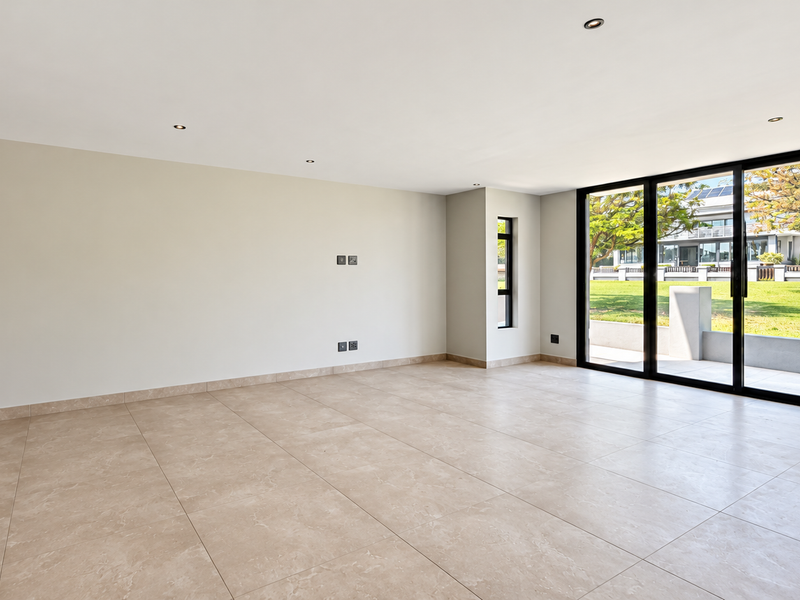 Spacious open-plan living area featuring large format floor tiles, recessed lighting, and expansive black aluminium sliding doors opening to a landscaped garden.