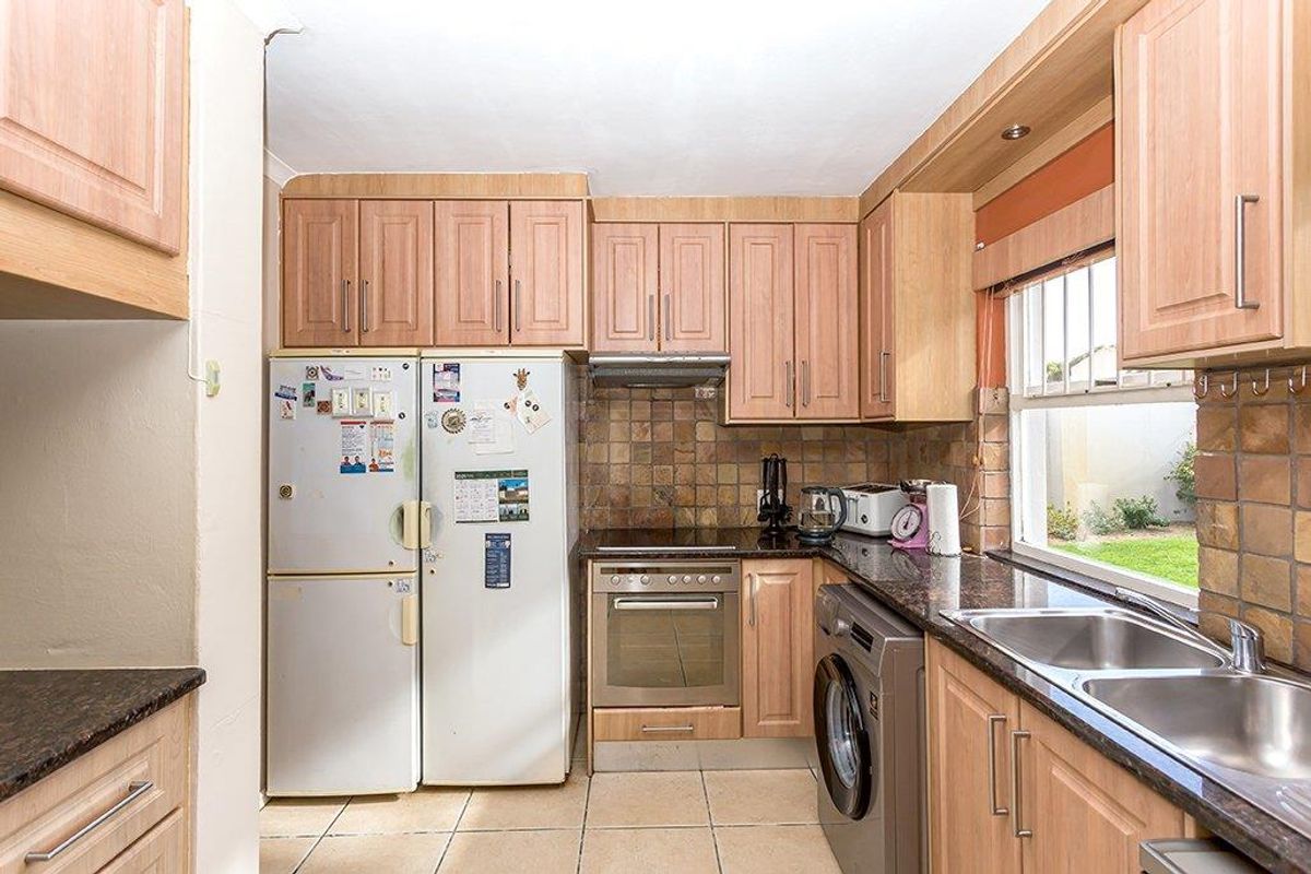 Functional kitchen featuring laminate cabinetry, granite countertops, built-in oven with hob, extractor fan, and tiled backsplash with integrated sink.