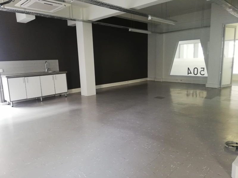Open-plan office space featuring a built-in kitchenette, ceiling-mounted air conditioning, and modern vinyl flooring with an industrial aesthetic.