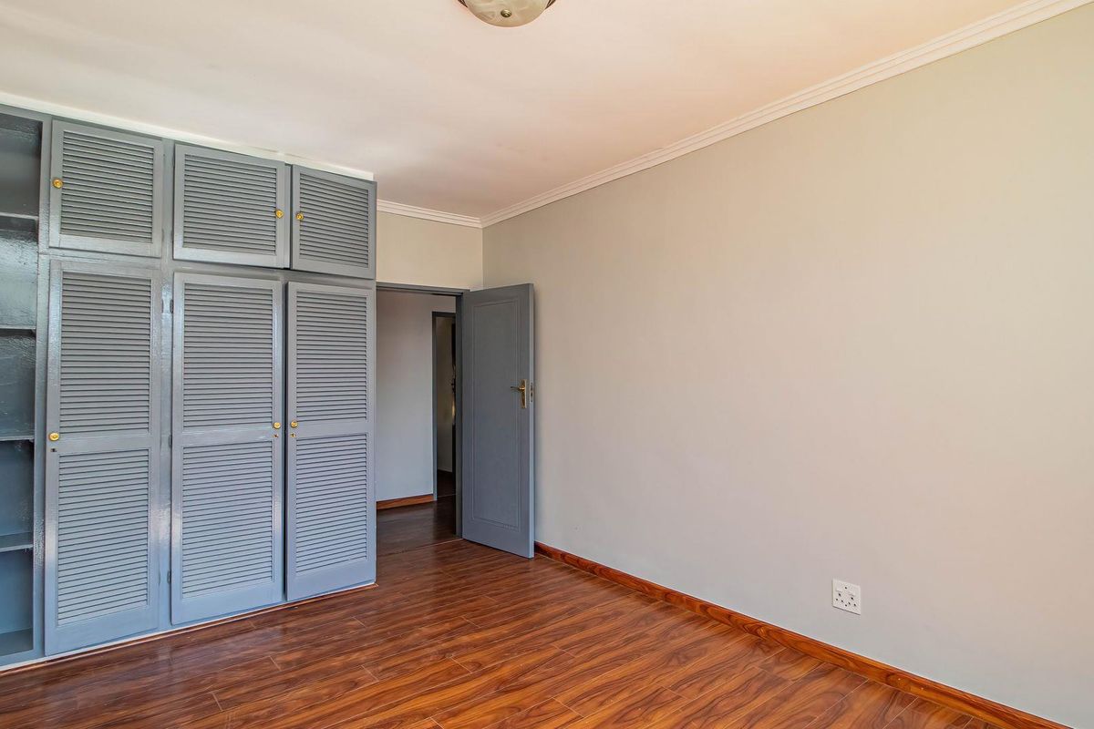 A clean, empty bedroom featuring laminate flooring, built-in louvered cupboards, and neutral wall finishes, offering a versatile space ready for personalization.