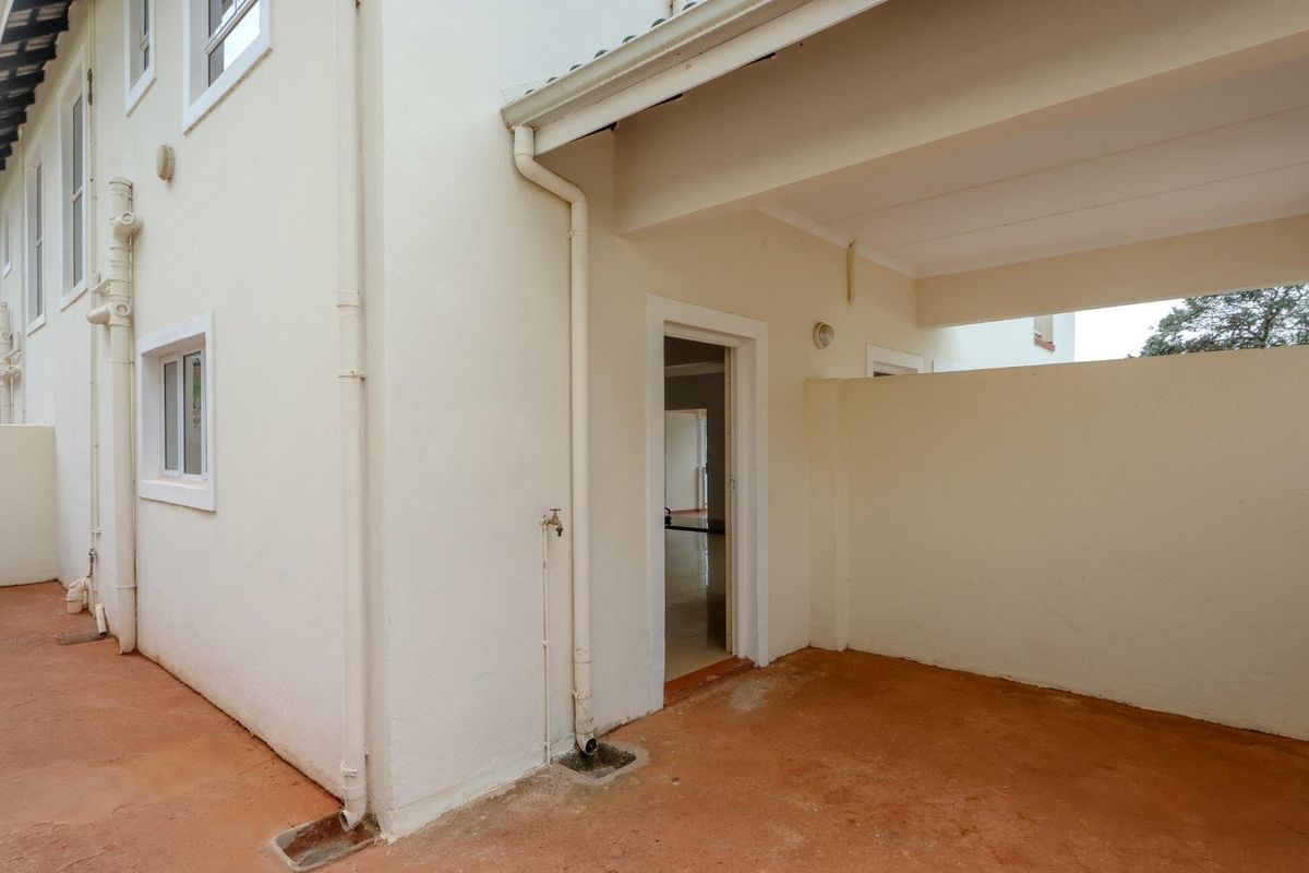 A rear exterior view of the townhouse featuring a covered patio area, external water tap, and concrete flooring.