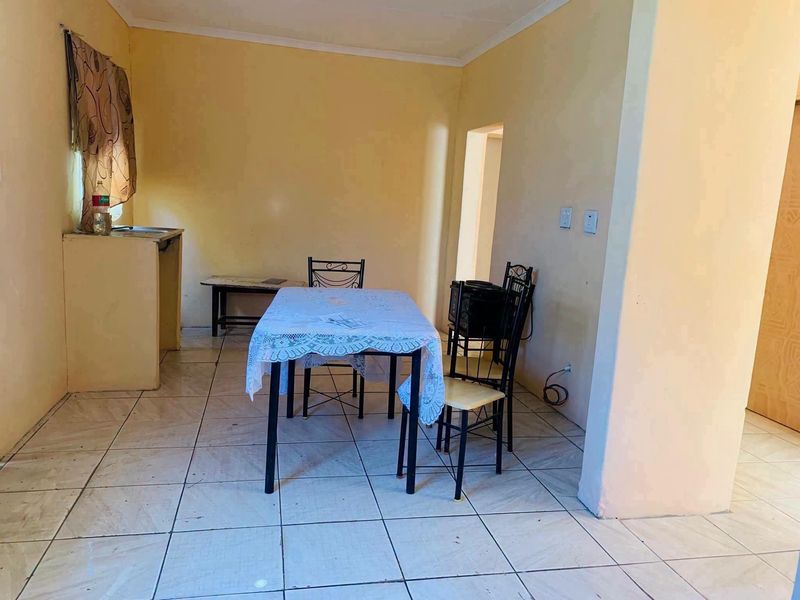 Open plan living and dining area featuring tiled flooring and a basic built-in sink unit, offering a functional space with potential for modernization.