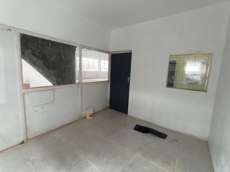 A vacant industrial office space featuring tiled flooring, internal glass partitions, and a solid core door, requiring minor cosmetic refurbishment.