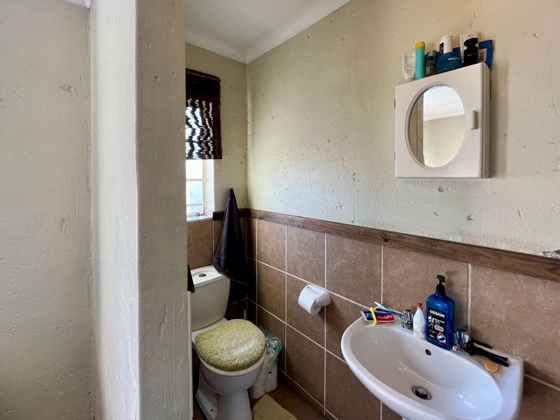 A compact bathroom featuring a pedestal basin, a standard toilet, and half-height wall tiling with a wooden trim finish.