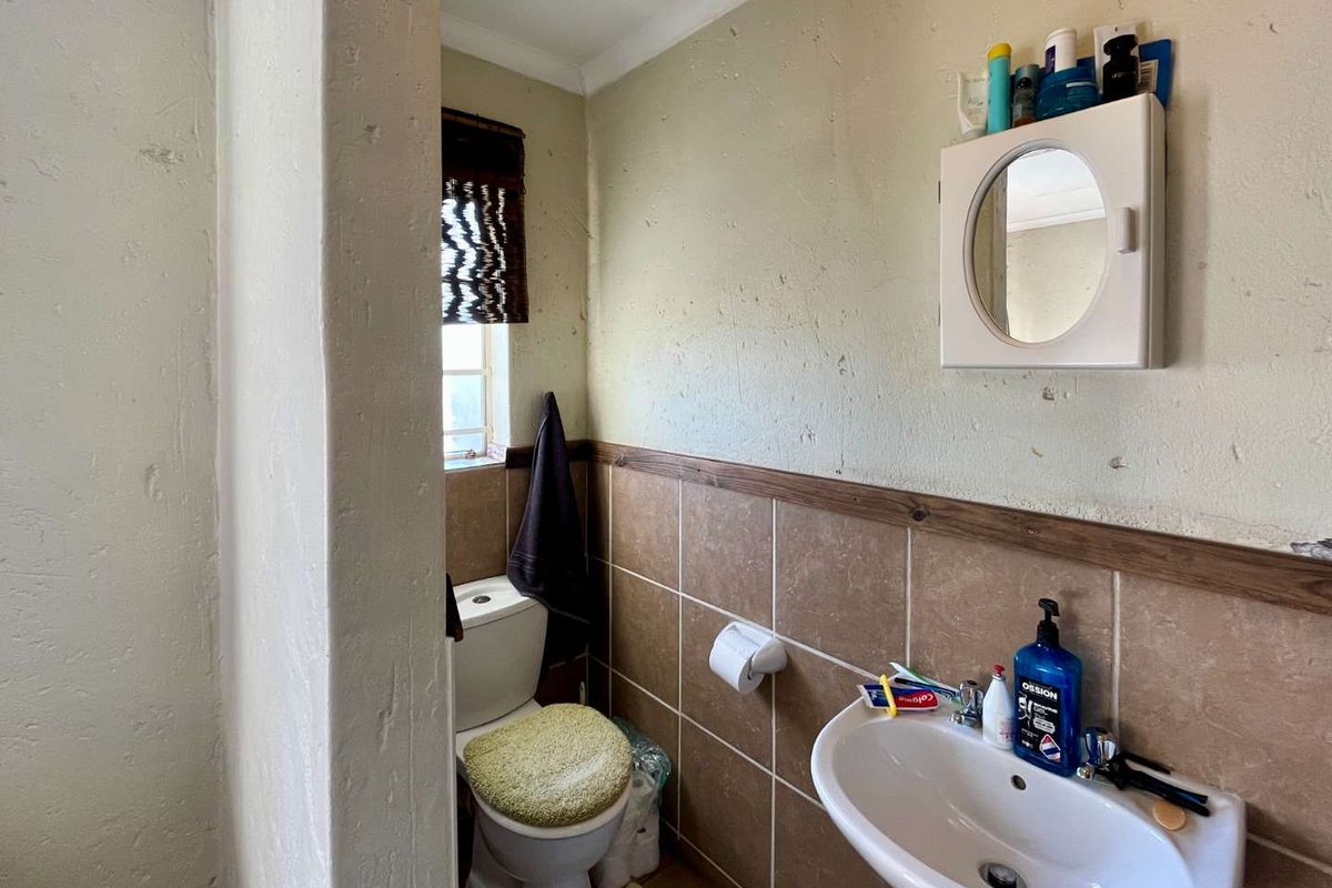 A compact bathroom featuring a pedestal basin, a standard toilet, and half-height wall tiling with a wooden trim finish.