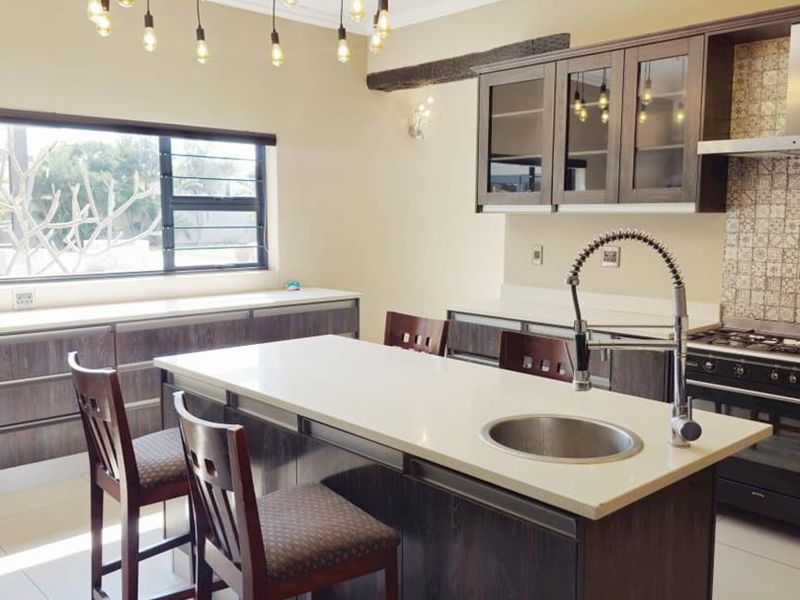 Modern kitchen featuring a central island with stone countertops, dark wood cabinetry, gas stove, and stylish pendant lighting.