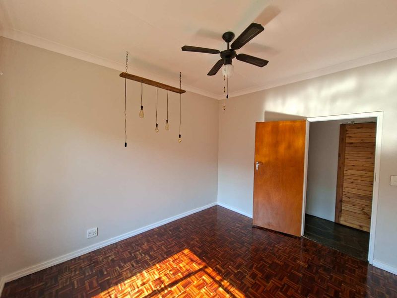 A bright, empty bedroom featuring polished parquet flooring, a ceiling fan, and neutral wall finishes, offering a clean canvas for personalization.