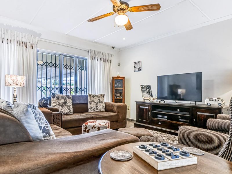 A comfortable living room featuring a ceiling fan, security gate, and sliding glass door providing access to the outdoor area.