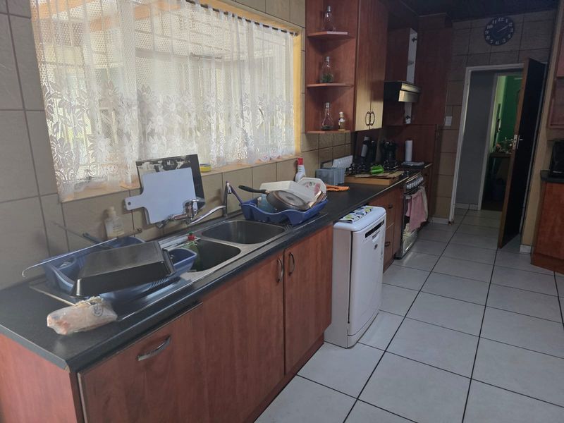 A functional kitchen featuring wooden cabinetry, tiled splashbacks, a double basin sink, and a freestanding oven with an extractor fan.