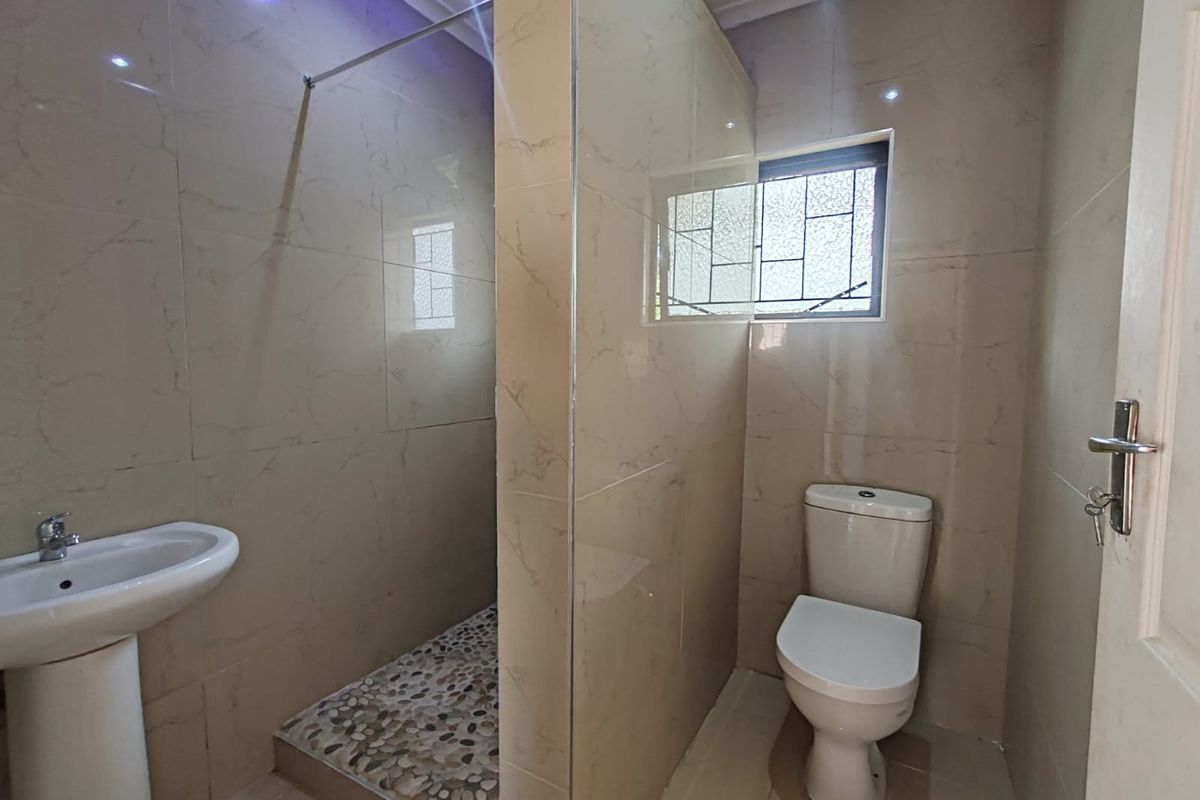 A modern, clean bathroom featuring a walk-in shower with pebble flooring, a pedestal basin, and a toilet, finished with neutral wall tiles.