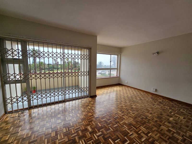 Spacious living area featuring classic parquet flooring, large windows for natural light, and a secure sliding door leading to an outdoor balcony.