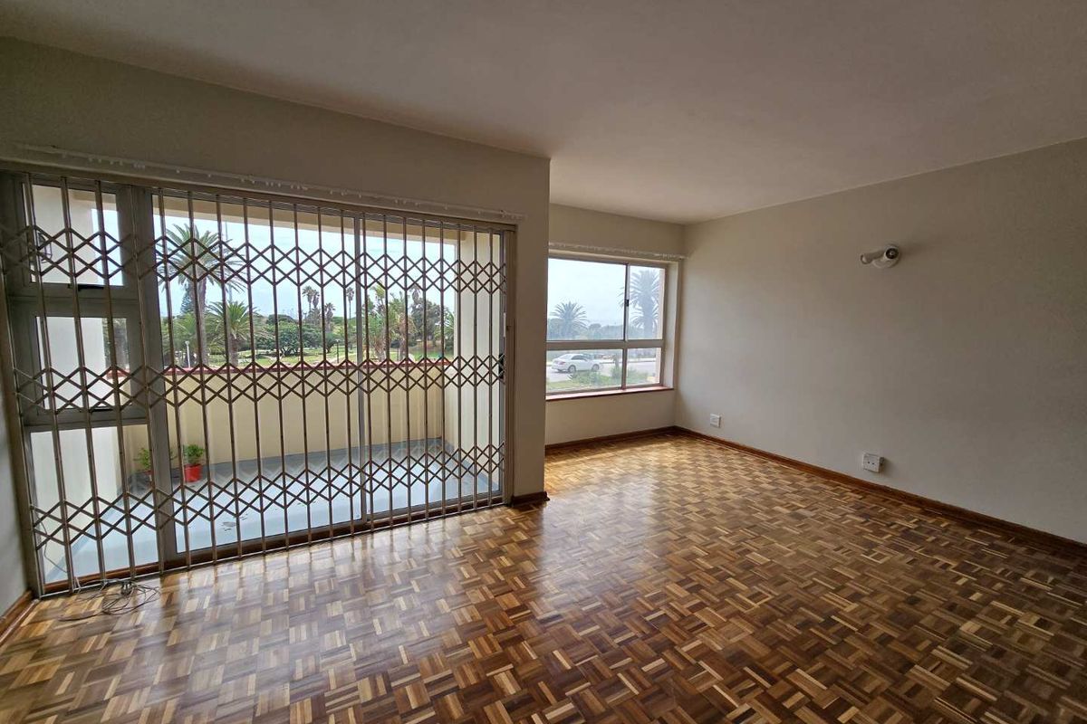 Spacious living area featuring classic parquet flooring, large windows for natural light, and a secure sliding door leading to an outdoor balcony.