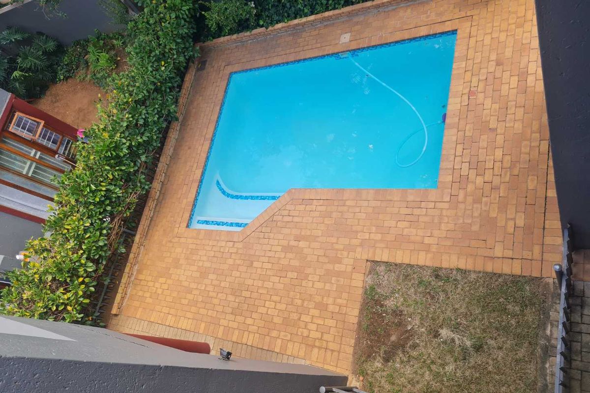 An elevated view of a private swimming pool area featuring brick paving, a perimeter wall, and established garden borders.