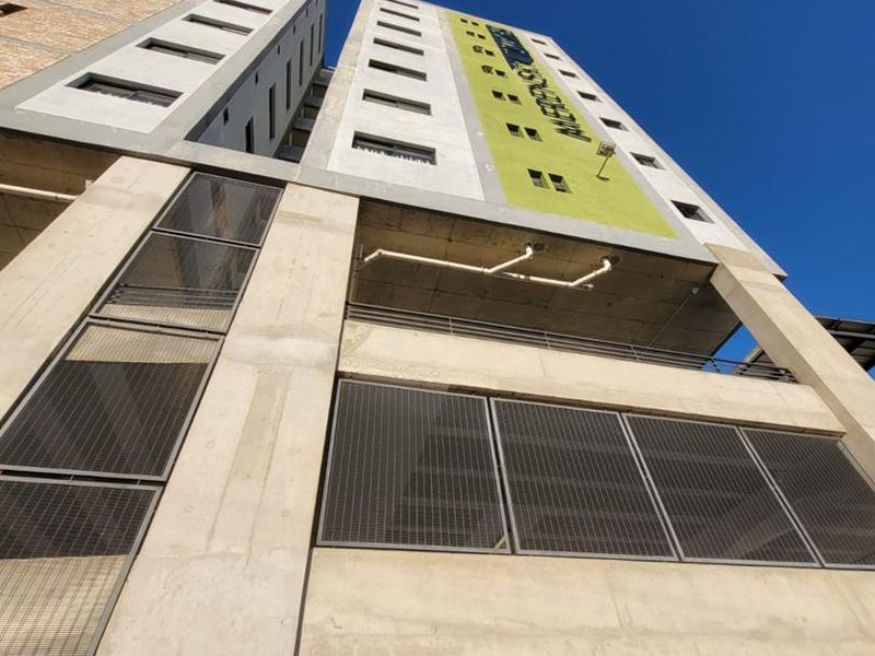 Low angle view of a modern apartment building facade featuring concrete construction, metal mesh detailing, and a designated vehicle height restriction entrance.