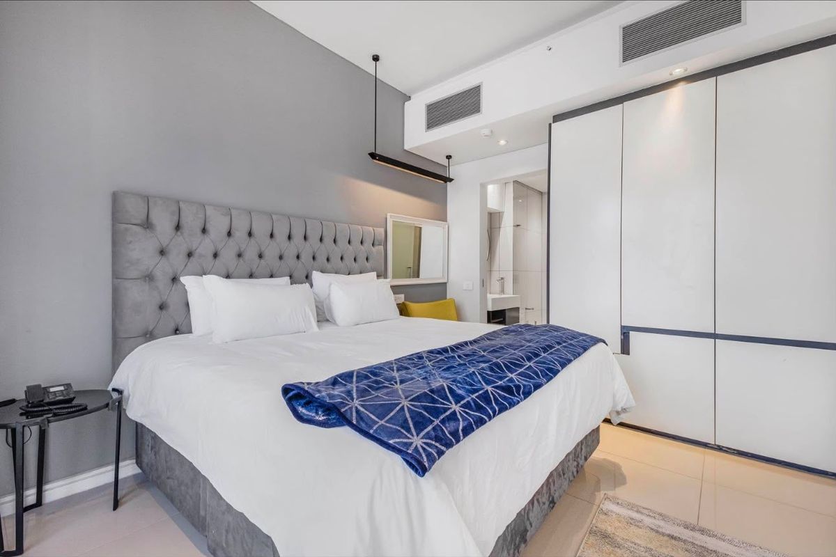 Modern bedroom featuring built-in cupboards, ducted air conditioning, and tiled flooring, with direct access to an en-suite bathroom.