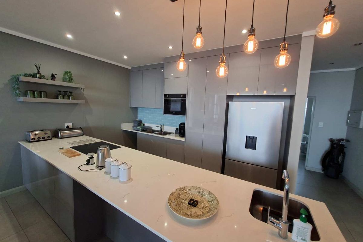 Modern kitchen featuring sleek grey cabinetry, quartz countertops, an integrated microwave, and stylish pendant lighting over a spacious island with an undermount sink.