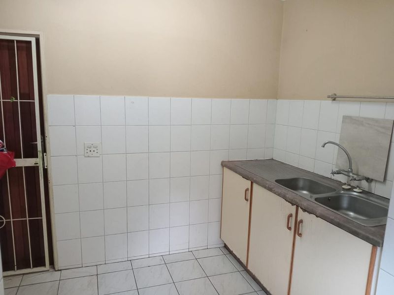 A functional kitchen area featuring a double bowl stainless steel sink, tiled splashback, and built-in base cabinetry with tiled flooring.