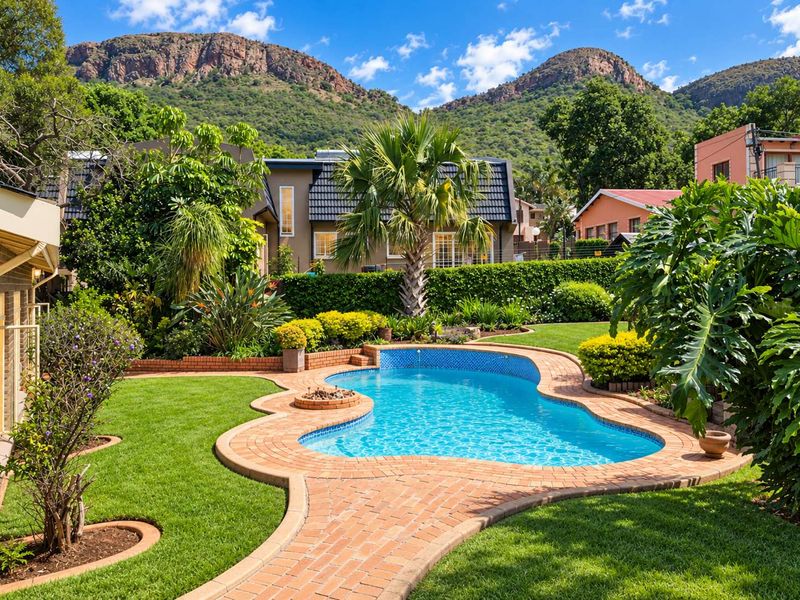 A beautifully landscaped backyard featuring a sparkling swimming pool, brick paved surround, and lush garden with mountain views.