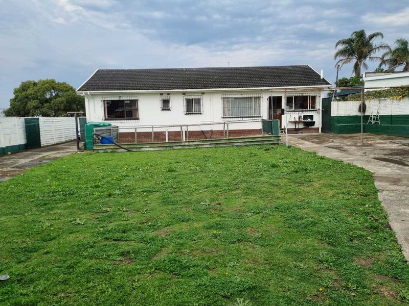 Rear view of the property featuring a large lawn, concrete driveway, and a single-story house with a tiled roof and security bars on windows.