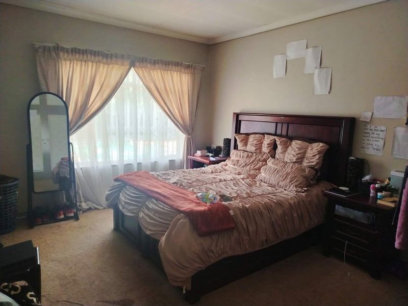 A standard bedroom featuring carpeted flooring and a window fitted with curtain rails and a security gate.