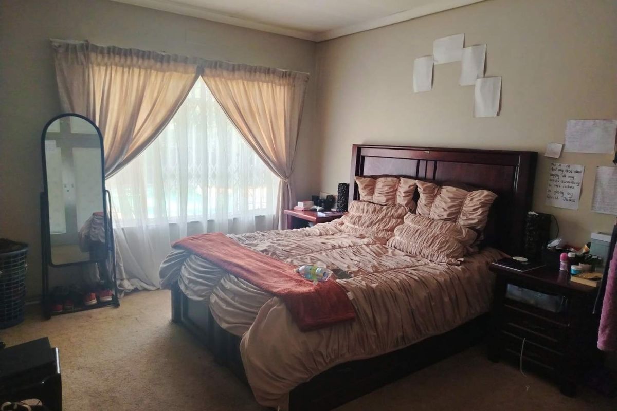 A standard bedroom featuring carpeted flooring and a window fitted with curtain rails and a security gate.