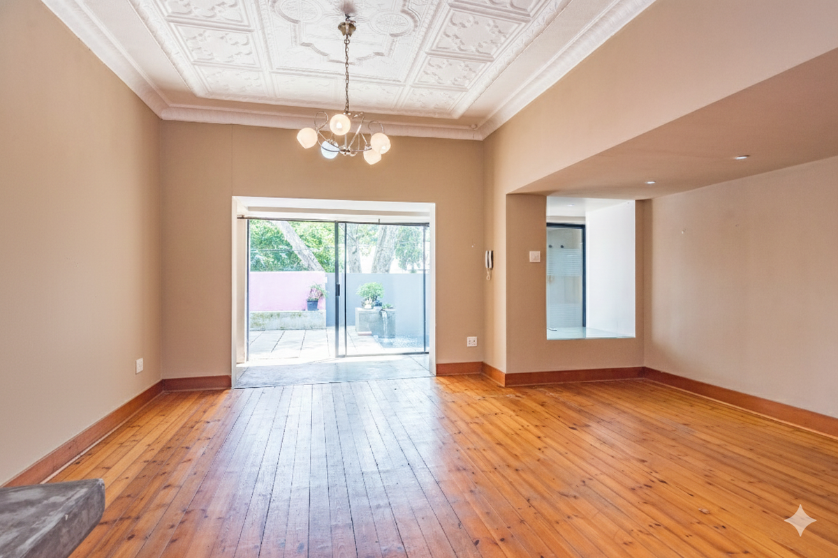Spacious living area featuring original hardwood flooring, an ornate plaster ceiling, and direct access to an outdoor patio through sliding glass doors.