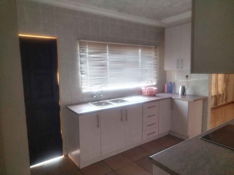 A functional kitchen featuring white built-in cabinetry, laminate countertops, a double sink, and tiled finishes, offering a clean and practical workspace.